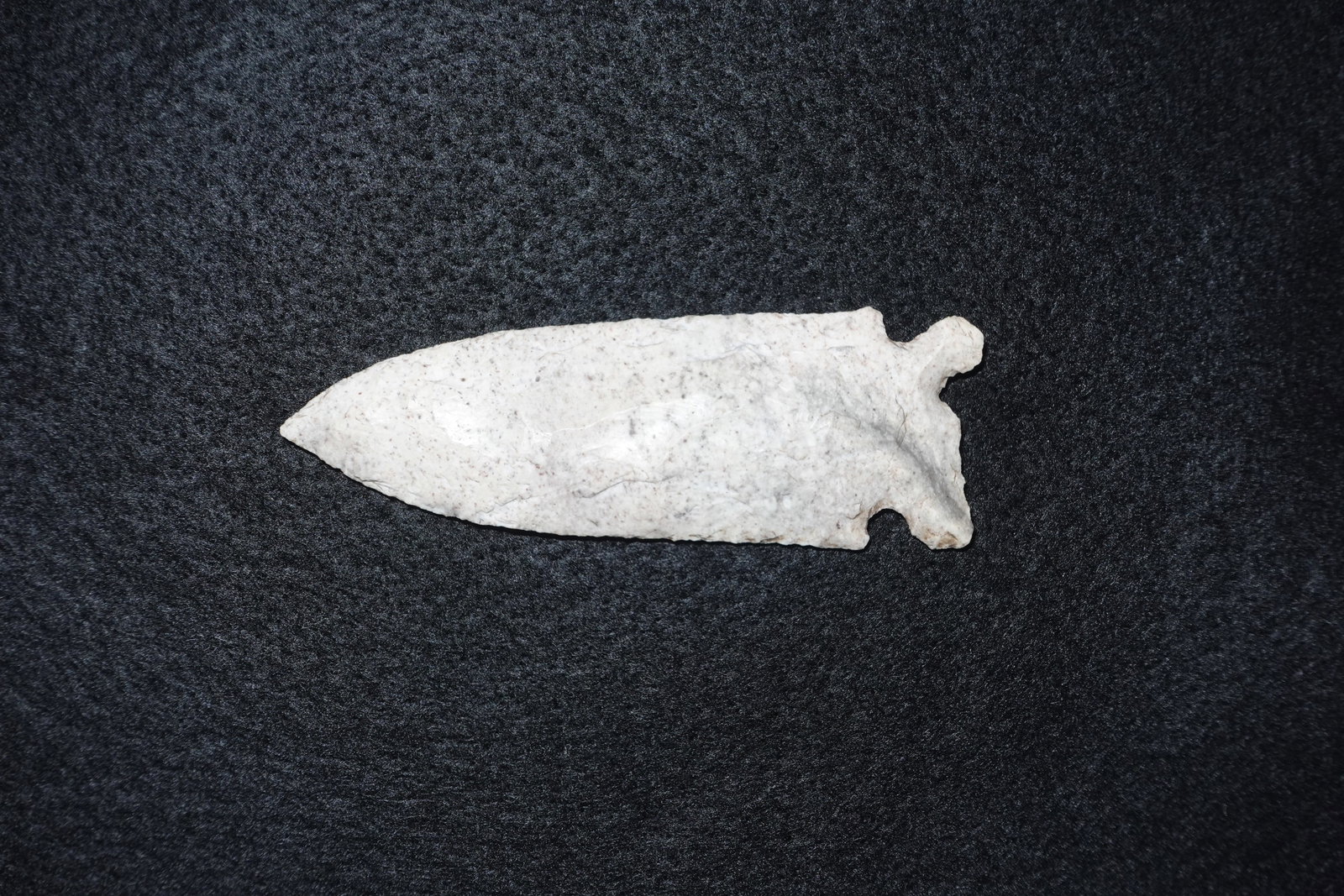 Graham Cave: Long lanceolate bifacial stone projectile point fashioned from light gray to white speckled chert or similar stone. Blade tapers to a fine tip and terminates in a pronounced basal notch with small