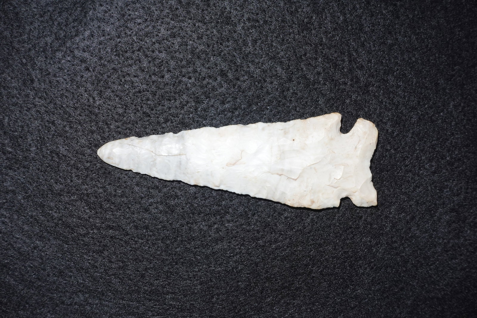 Graham Cave: Elongated white-to-cream flaked stone projectile point with a long triangular blade and thin, flattened profile. Basal notches create pronounced ears at the hafting end and fine edge retouch runs