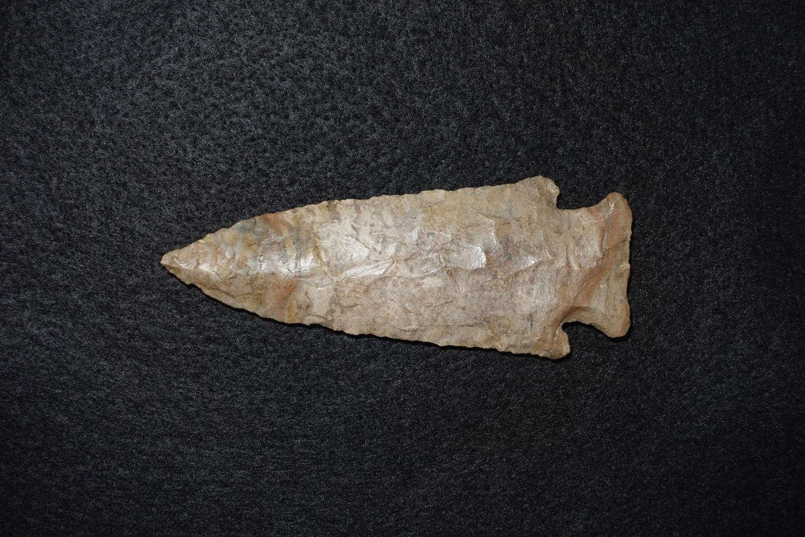 Hardin: Flaked stone projectile point with a narrow, tapered blade, pronounced barbed shoulders and a notched stem. Banded tan-to-light-brown coloration shows glossy flake scars and fine edge-retouch along