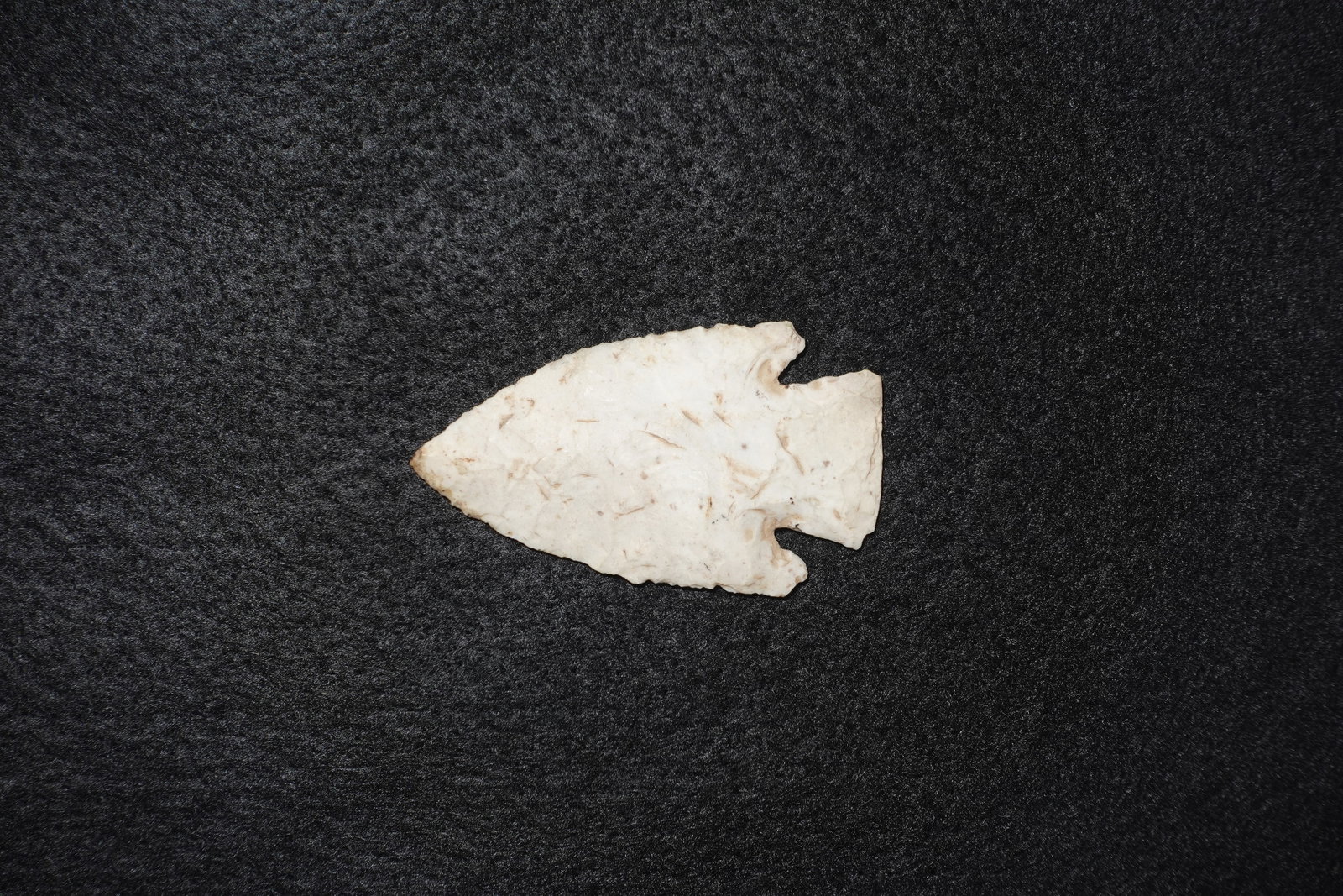Hardin: Cream to off-white flaked stone projectile point with a broad triangular blade, deep side notches and a defined stemmed base. Fine flake scars and pressure retouch along the edges create a slightly