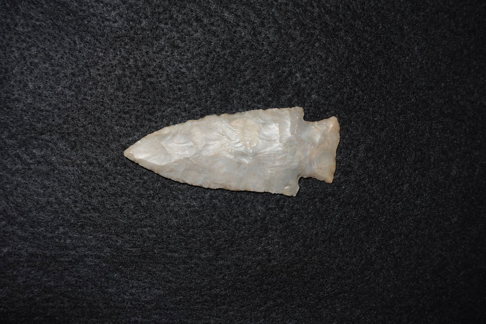 Hardin: Light gray flaked stone projectile point with a lanceolate outline and narrow stem featuring small basal notches. Bifacial flaking displays pronounced rippled flake scars and a slightly translucent,