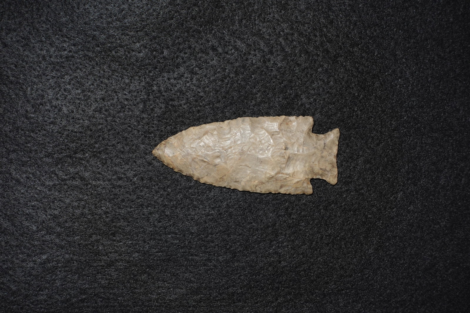 Hardin: Light tan-to-cream chert projectile point with pronounced bifacial flaking across the blade. Leaf-shaped profile terminates in a narrow tip with fine denticulated edging and a notched basal stem with