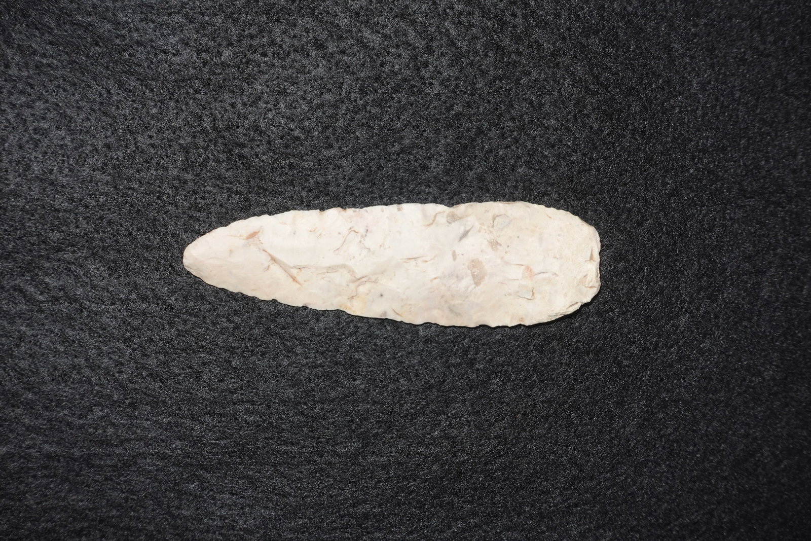Angostura: Elongated, leaf-shaped flaked stone projectile point with a narrow tapered tip and finely retouched edges. Crafted from light cream to off-white chert or similar siliceous material, the piece