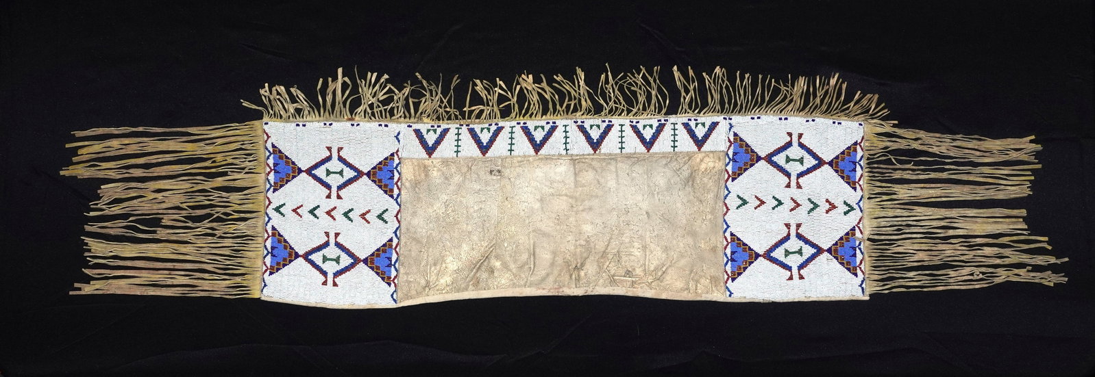 Sioux Beaded Saddle Bags: Beaded saddle bags with a dense white seed-bead ground and repeating geometric motifs in blue, green, red and purple. Long split-leather fringe trims both sides and ends while cloth binding secures th