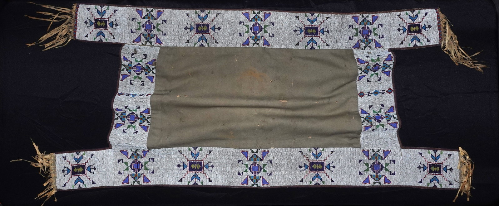 Sioux Beaded Saddle Blanket: Beaded saddle blanket with wide hand-stitched borders of white seed beads accented in blue, purple, green, red and yellow forming geometric starburst motifs. Central olive-green cloth panel is bordere