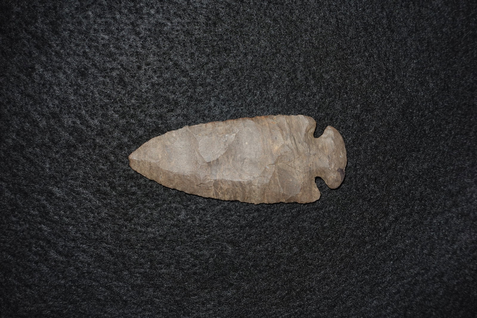 Dovetail: Bifacially flaked stone point with a pronounced dovetail-style notched base and distinct flake scars across both faces. Brown-gray chert material with an elongated, leaf-shaped blade and a narrow stem