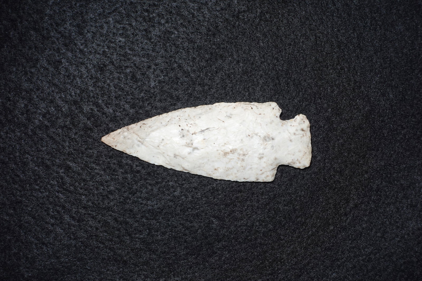 Etley: Creamy white chert projectile point with bifacial flake removal producing a long, narrow triangular blade and a sharp tip. Basal notching with a small ear at the stem area and fine edge retouch along 