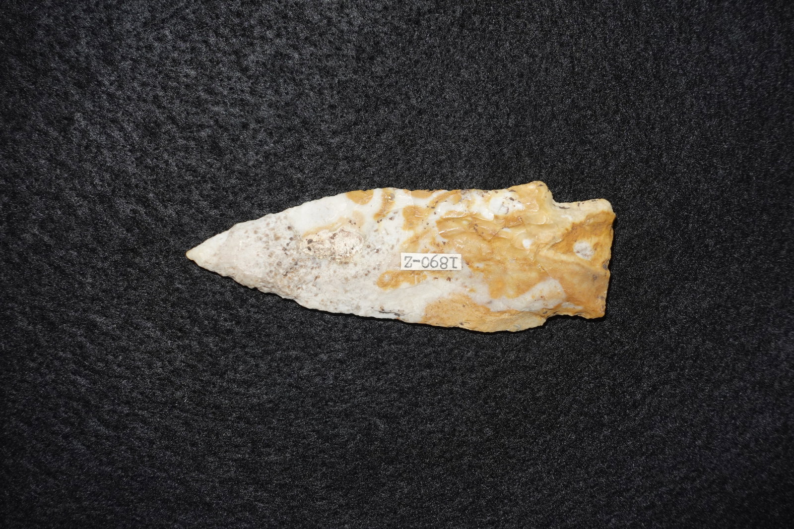 Etley: Lanceolate bifacial stone projectile point with an elongated triangular blade and sharply tapered tip. Crafted from cream-to-tan chert with white quartz veining and orange-brown patina, exhibiting
