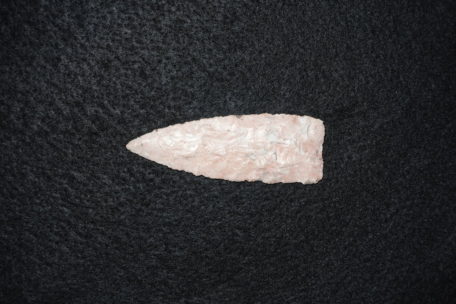 Carter Blade: Elongated bifacial stone blade with a tapered point and a broad, squared base. Light pink to tan material displays dense, fine flaking with overlapping flake scars across both faces and subtle gray st