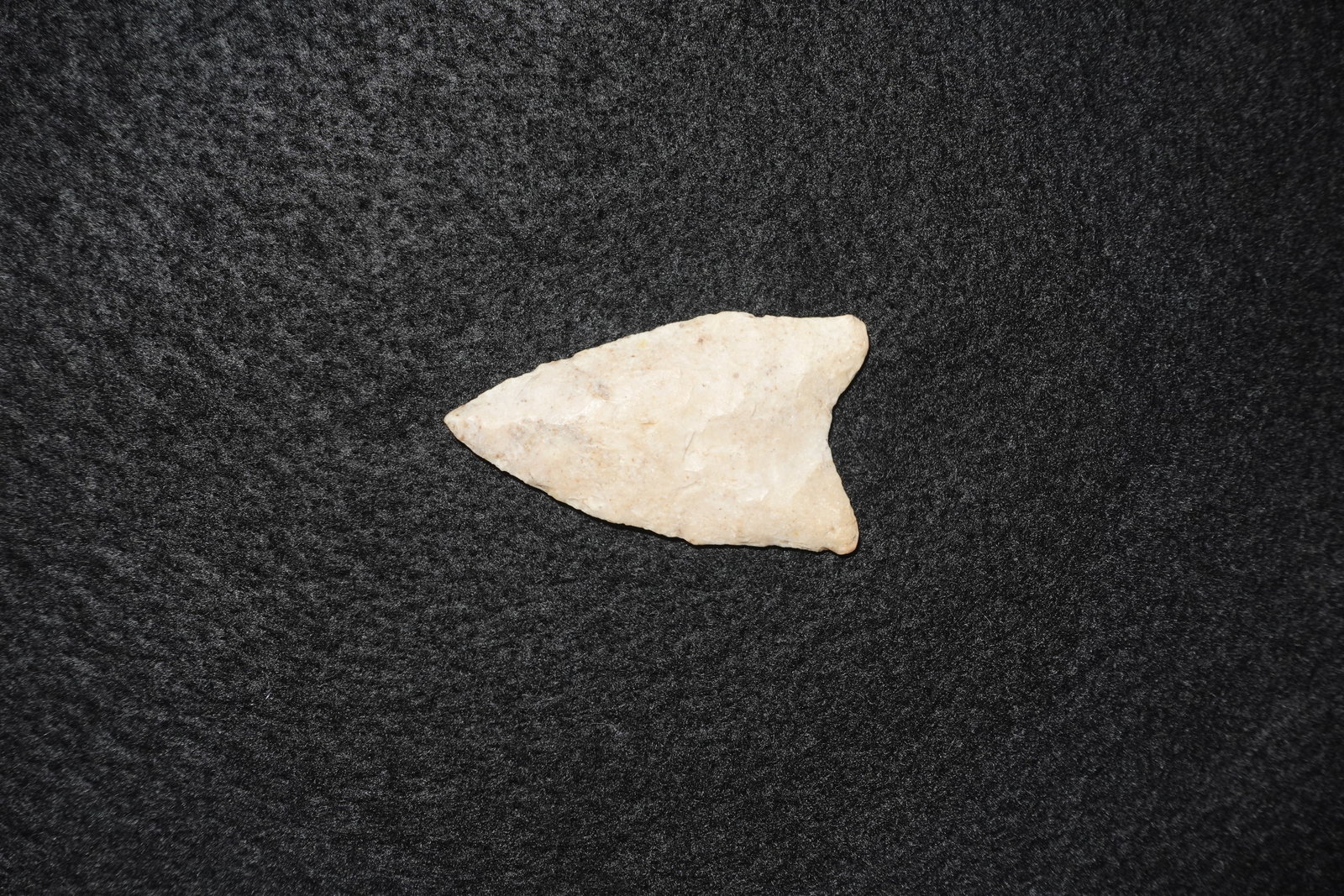 Dalton: Cream-colored flaked stone projectile point with a triangular blade and bifacial flaking along the faces. Thin, worked edges and subtle basal notches exhibit percussion and pressure flake scars. A