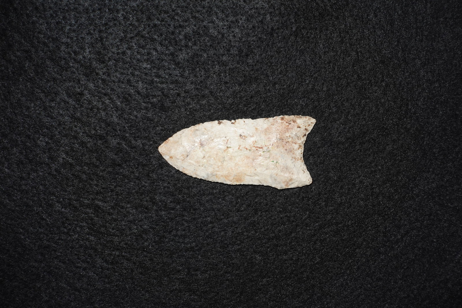 Sloan: Flaked stone projectile point in a light cream to tan color with areas of brown staining and residual cortex. Bifacial flaking along the blade shows fine pressure work and a tapered, lanceolate