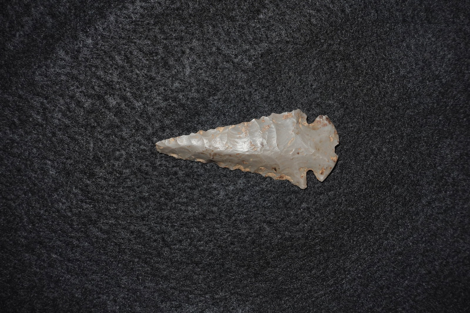 Dovetail: Light gray chert projectile point with pronounced bifacial flaking and a tapered blade culminating in a sharp tip. The base shows distinct dovetail-style notches with ear-like projections and tan
