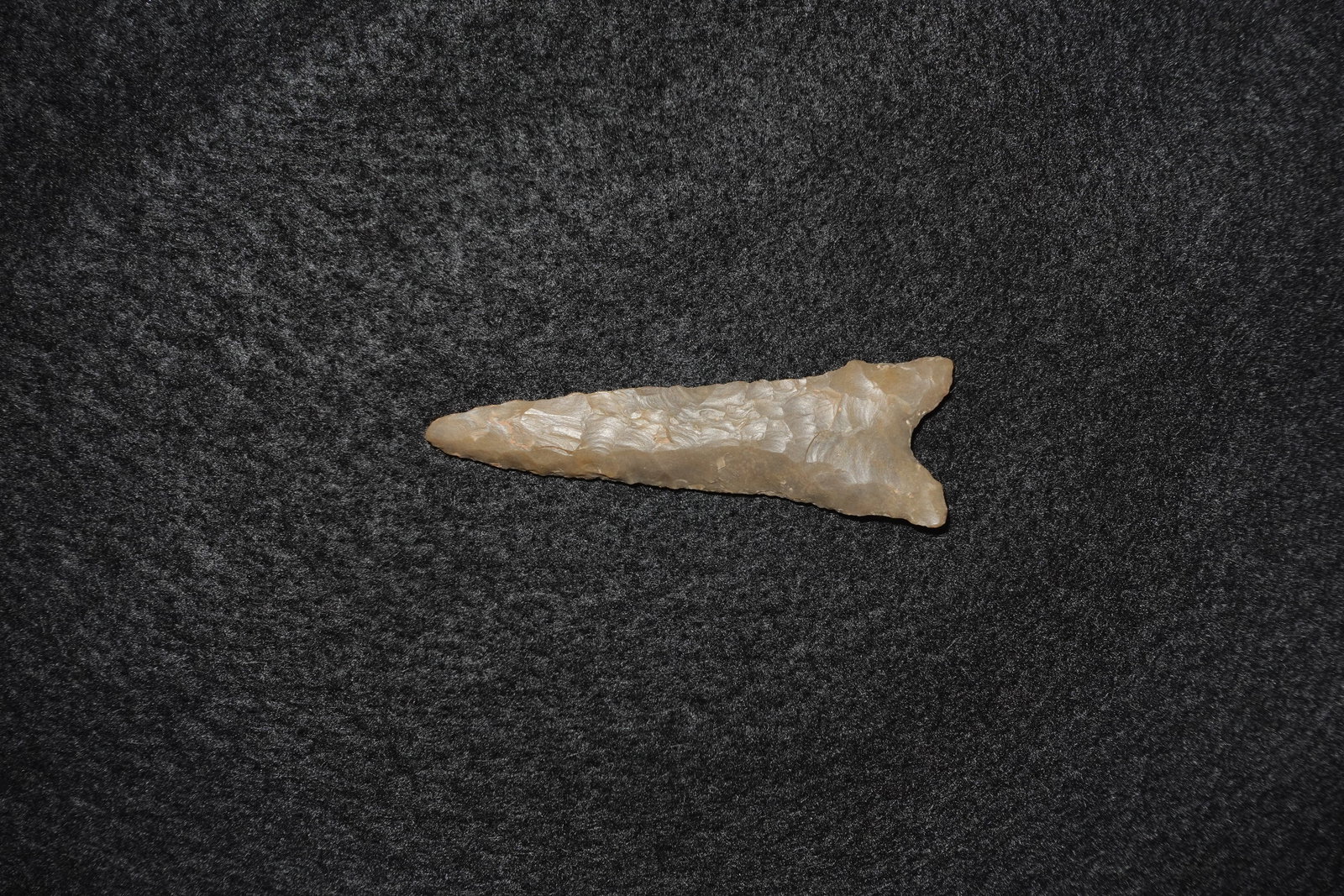 Dalton: Elongated leaf-shaped flaked stone projectile point with a pronounced bifurcate (two?pronged) base and narrow tapered blade. Light tan to beige translucent stone with visible flake scars and fine pres
