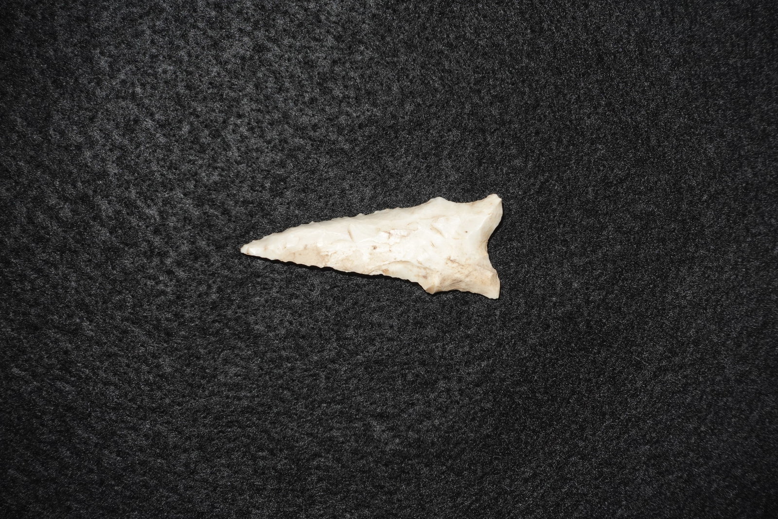 Dalton: White-to-cream flaked stone projectile point with a triangular blade and shallow notches at the base. Bifacially worked with visible pressure-flake edge detailing and a thin, well-defined tip. Light s