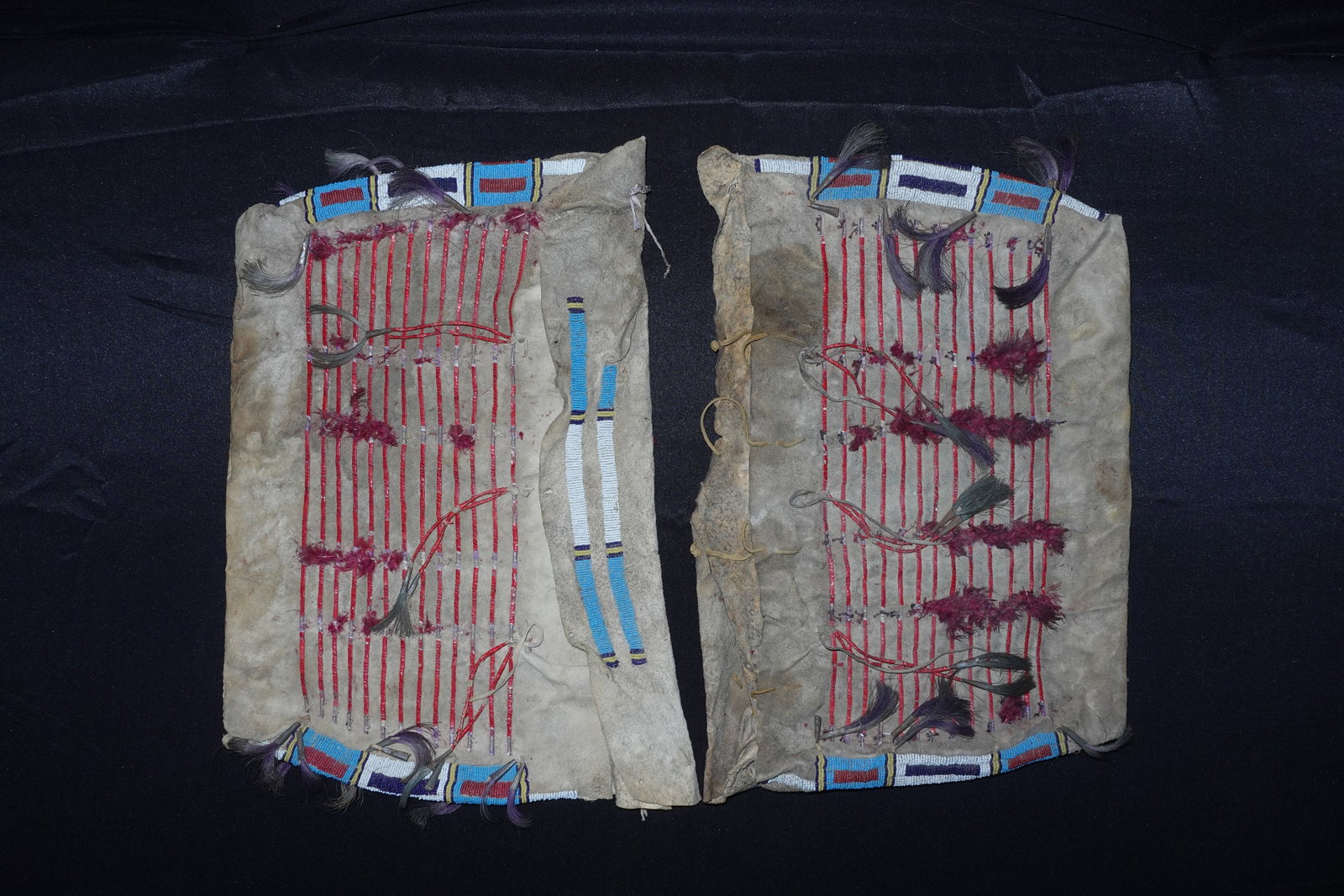 Matching Cheyenne Possible Bags: Cheyenne-style hide bags decorated with horizontal red quillwork strips, clusters of purple feather tufts and long horsehair tassels. Upper edges feature geometric glass beadwork in blue, white, red