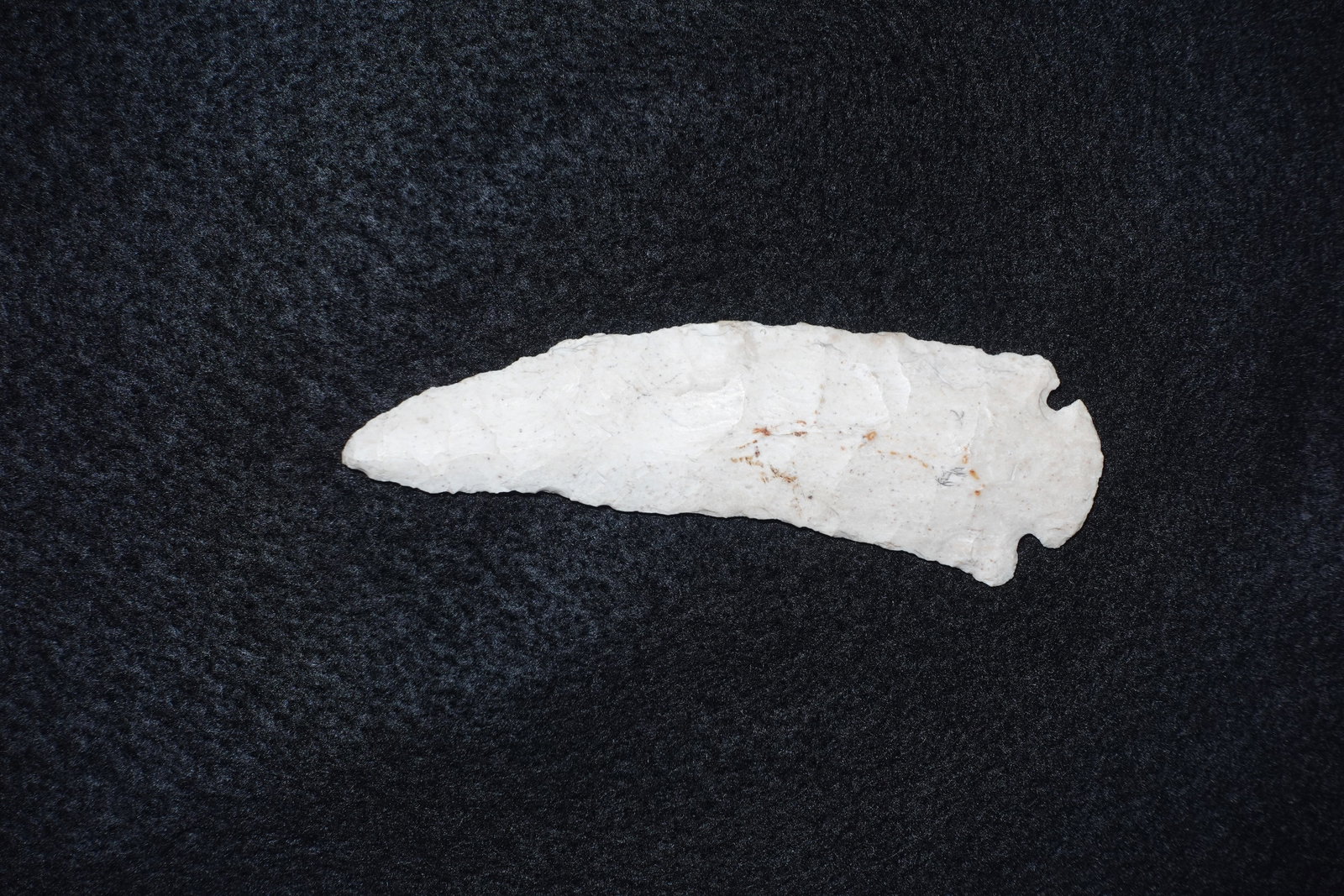 Dovetail Knife: Bifacially flaked white chert knife with a long tapered blade and a pronounced dovetail-style basal notch. Fine percussion and pressure flake scars cover both faces with occasional brown mineral stain