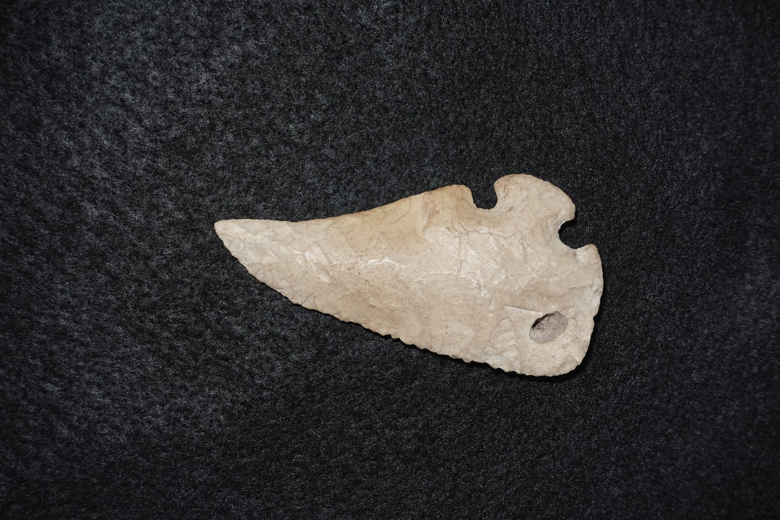 Corner Tang Knife: Light beige hand-flaked stone knife with a pronounced corner tang and deep notches at the base. Blade exhibits stepped flaking and a serrated distal edge, with a small circular perforation near the ta