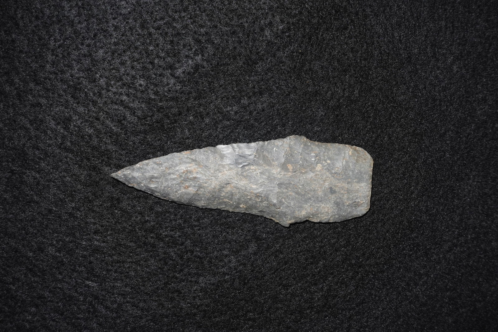 Scottsbluff: Lanceolate flaked stone point with a long triangular blade and a sharply tapered tip. Gray chert/flint exhibits repeated percussion and fine retouch flake scars on both faces with subtle mineral