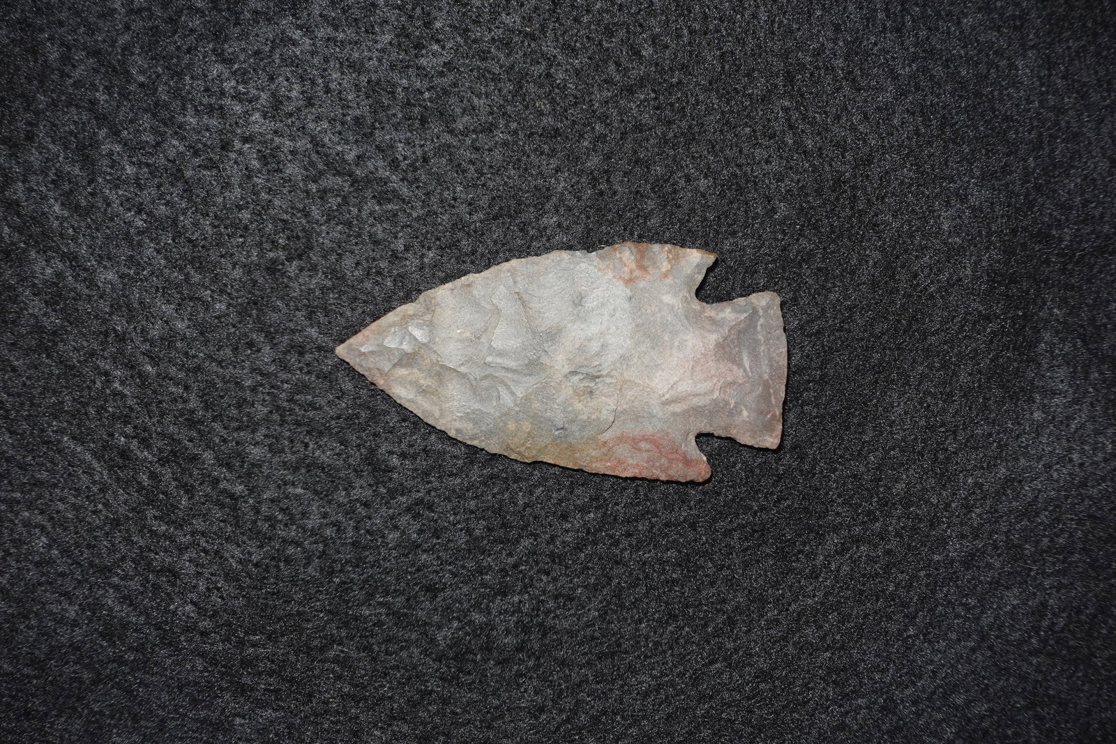 Apple Creek: Gray-brown flaked stone projectile point with a pronounced notched base and broad triangular blade. Bifacial flaking displays overlapping percussion and pressure flake scars across the faces, with