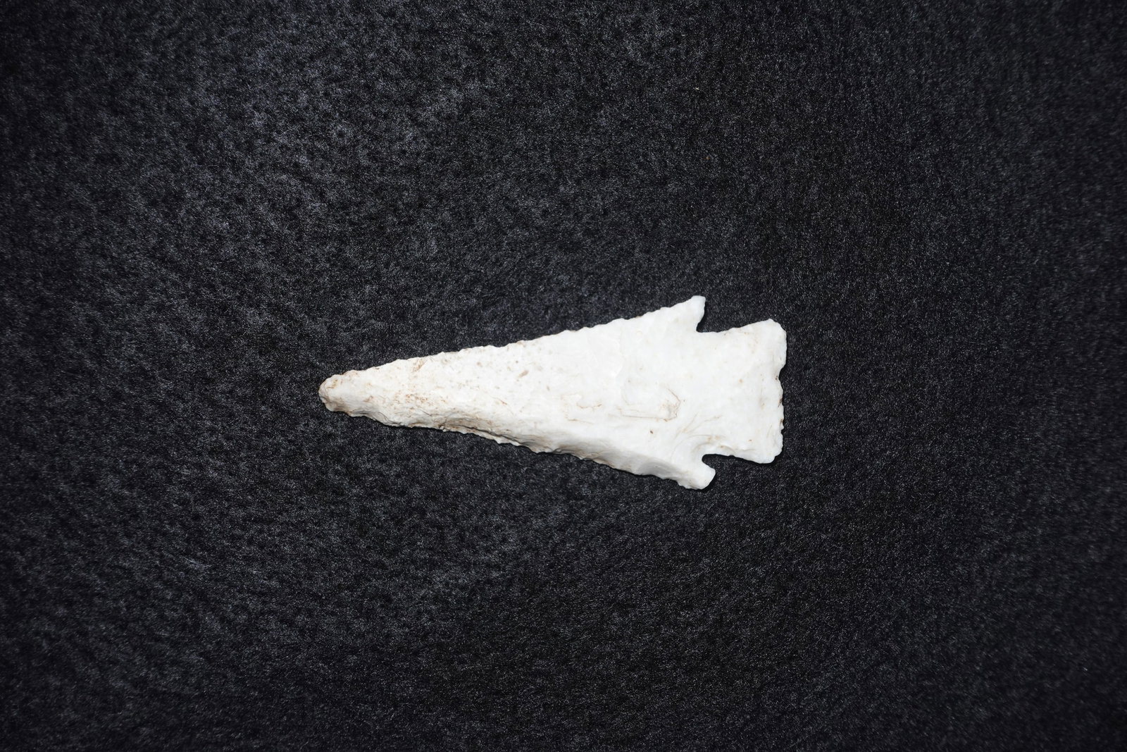 Hardin: White flaked stone projectile point with an elongated triangular blade and visible percussion flake scars on both faces. Broad basal area features two pronounced notches at the shoulders and a