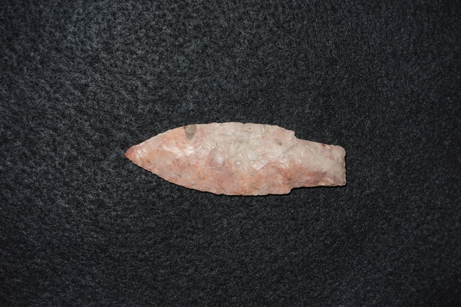 Kramer: Elongated leaf-shaped flaked stone blade in pink-peach tones with scattered white and brown mineral patches. Bifacially worked surfaces exhibit fine pressure flaking along the edges and a tapered tip
