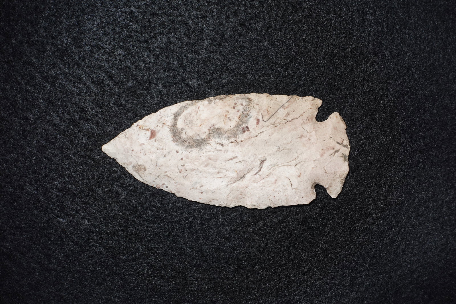 Hopewell: Leaf-shaped flaked stone projectile point made from light cream chert with reddish flecking and gray mineral staining. Blade exhibits extensive flake scars and fine pressure flaking with shallow side