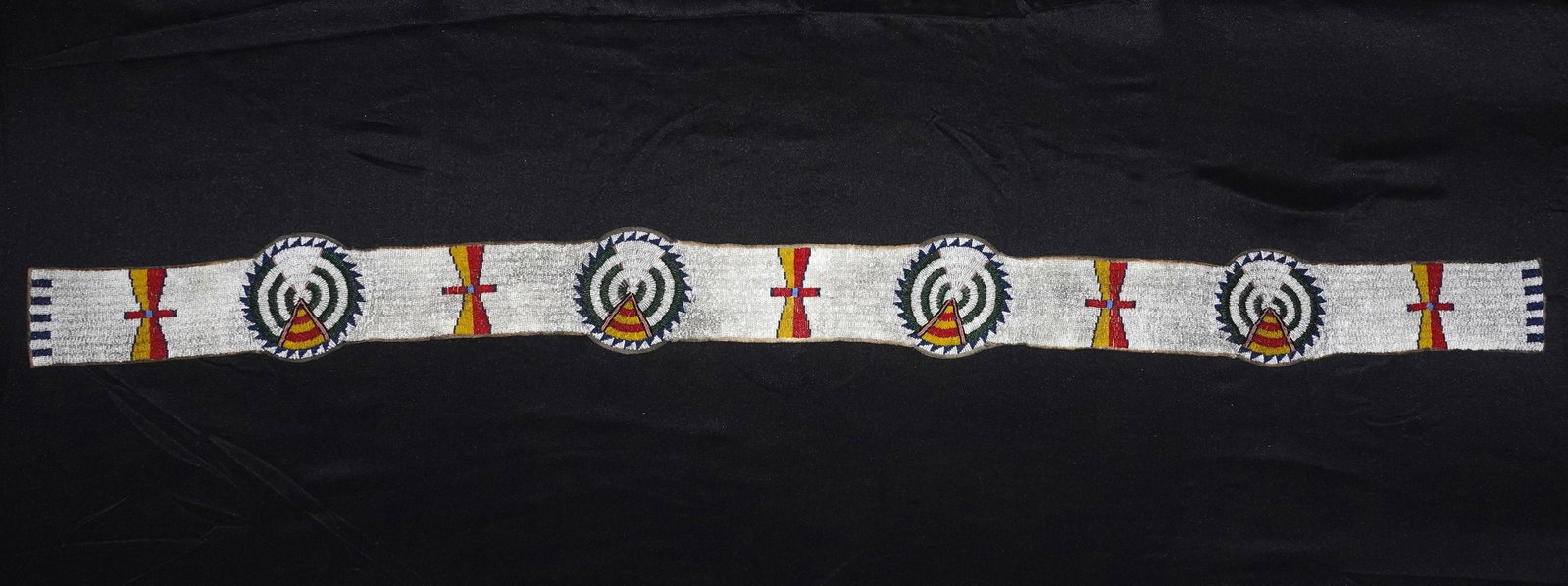 Beaded Blanket Strip: Hand-sewn beaded blanket band with a white seed-bead ground and repeating circular medallions of concentric green rings, blue sawtooth edging and central striped triangular motifs in red and yellow.