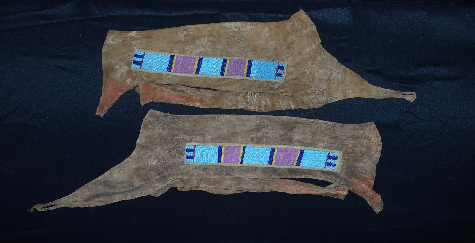 Early Crow Leggings: Tanned hide leggings with long rectangular bead panels sewn to cloth backings. Beadwork features light turquoise, lavender, cobalt blue and yellow glass beads arranged in vertical stripe bands with na