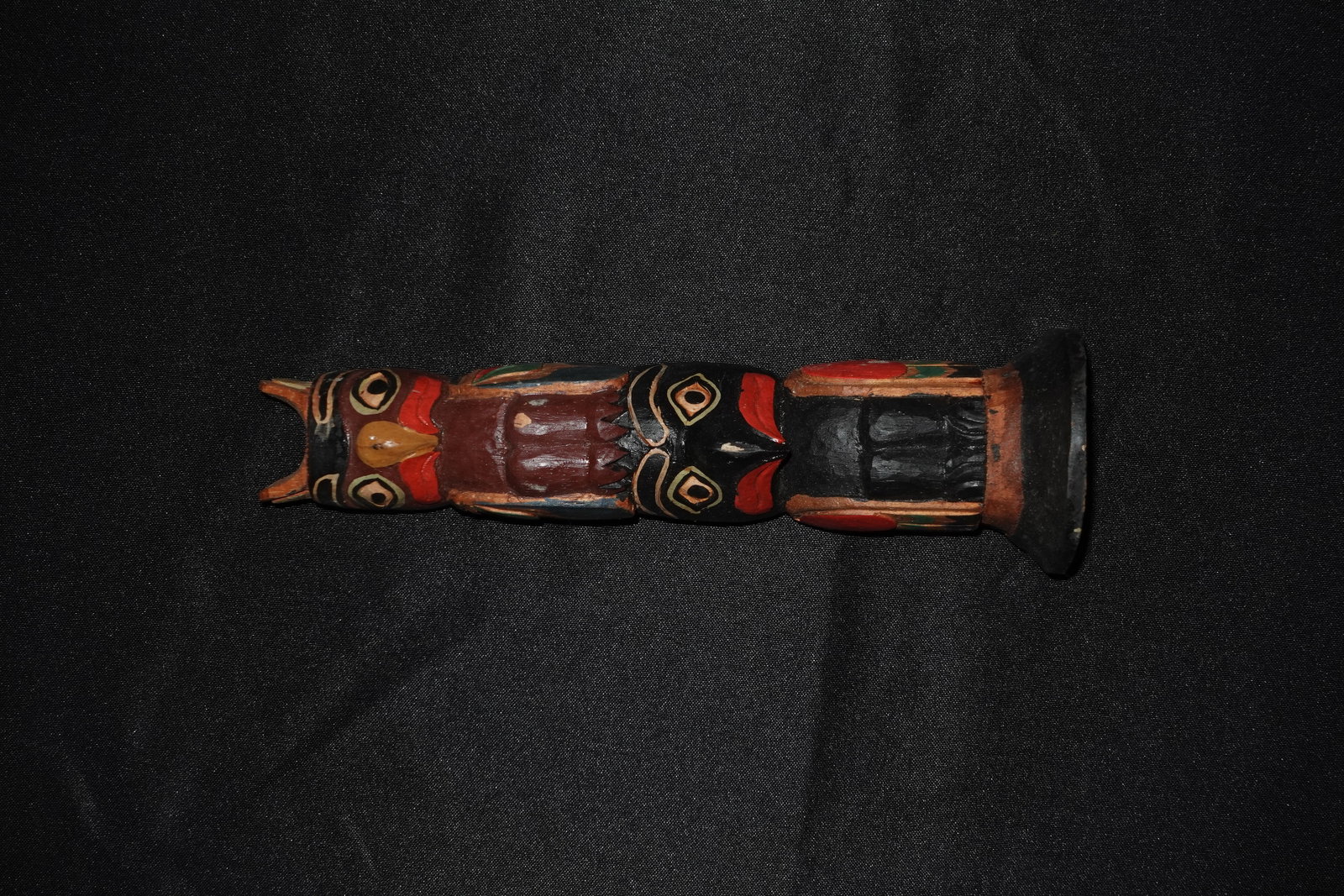 Carved NW Coast Totem: Hand-carved wooden totem-style carving with stacked stylized animal faces and geometric motifs. Polychrome paint in red, black, green and natural wood tones highlights carved round eyes, beak-like