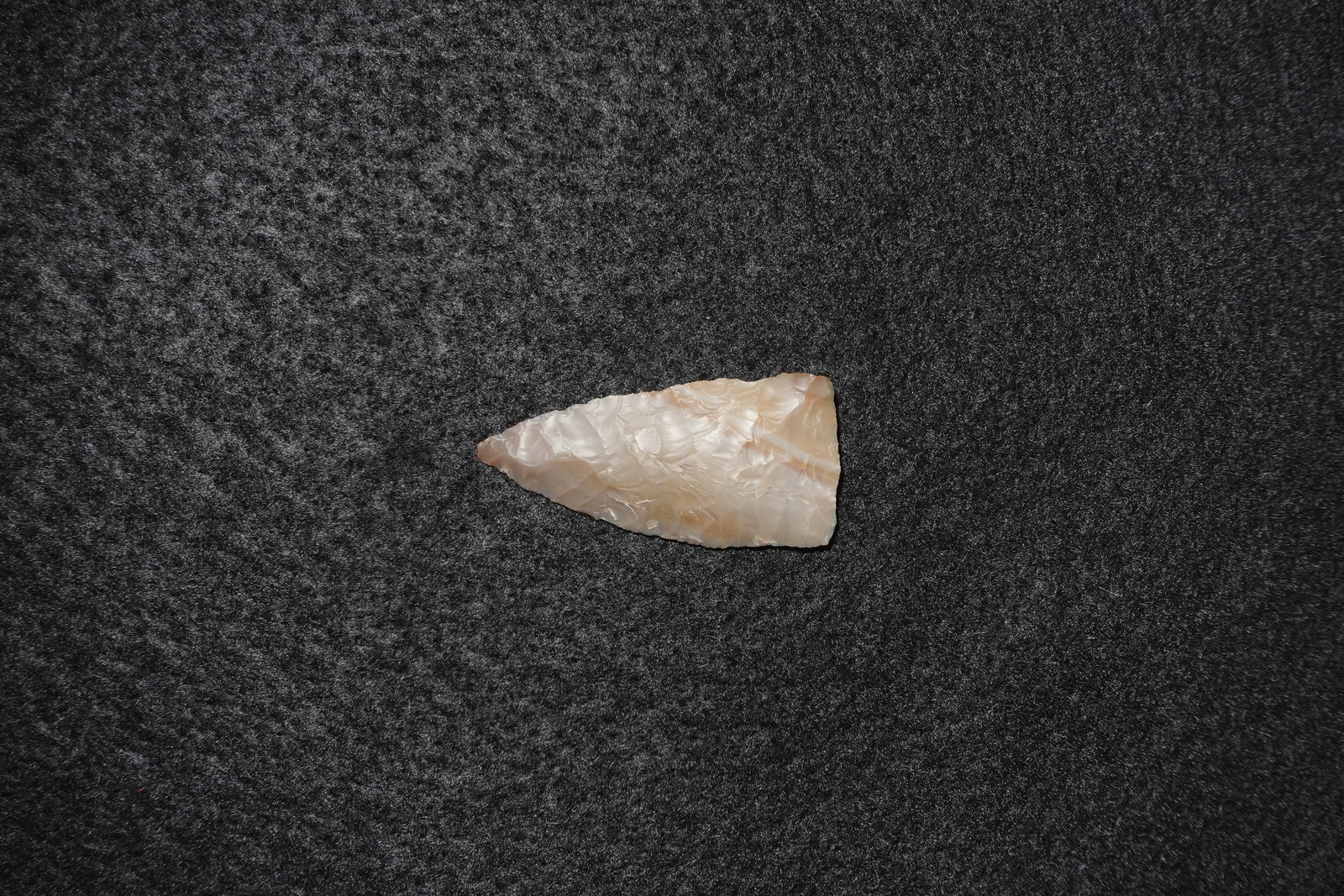 First View: Light translucent cream-to-tan flaked stone projectile point with a triangular blade and pronounced stepped flake scar pattern across the surface. Fine edge retouch culminates in a sharp tip and a str