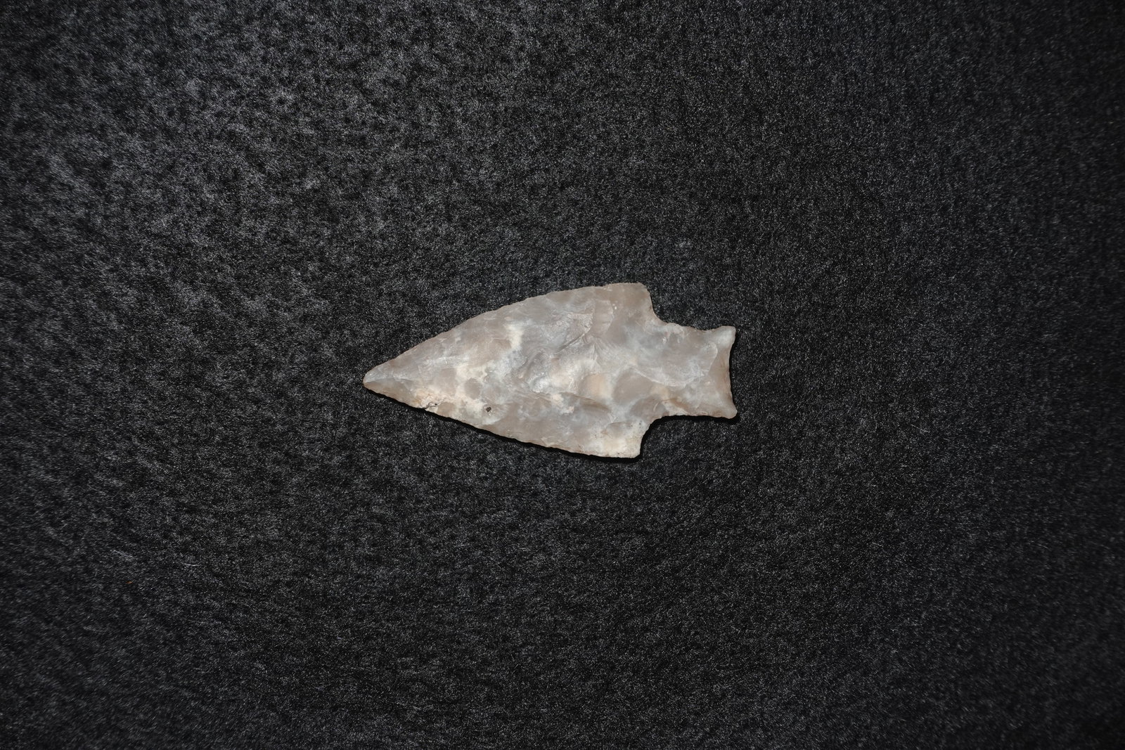 Agate Stemmed Point: Stemmed point fashioned from translucent agate with pale gray and tan tones. Bifacial flaking across both faces produces a sharp triangular blade and a narrow stem with a small basal notch. Fine