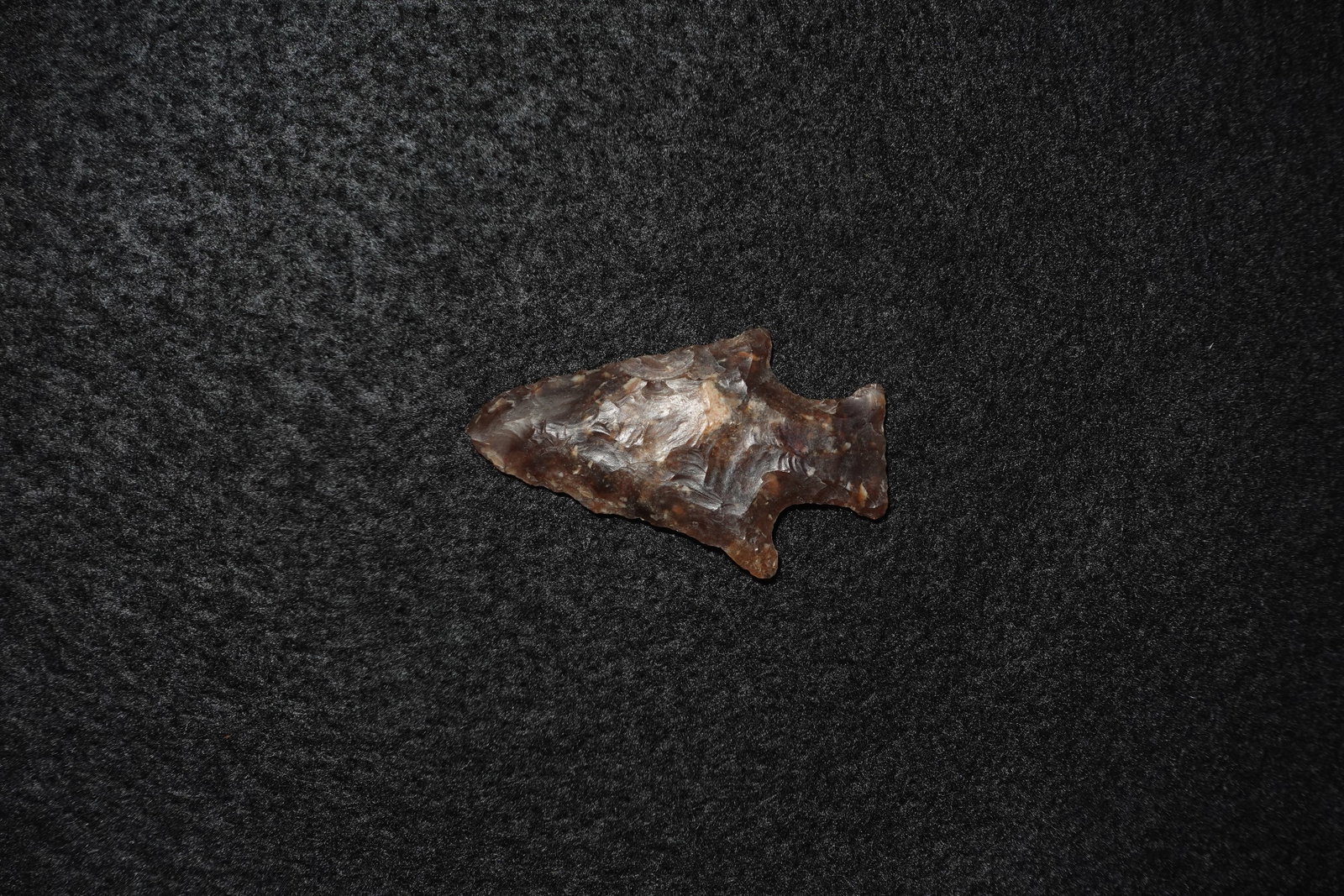 Knife River Stemmed Point: Stemmed stone projectile point crafted from dark translucent brown chert with lighter tan mottling. Bifacial knapping produced pronounced conchoidal flake scars and stepped ripple patterns across