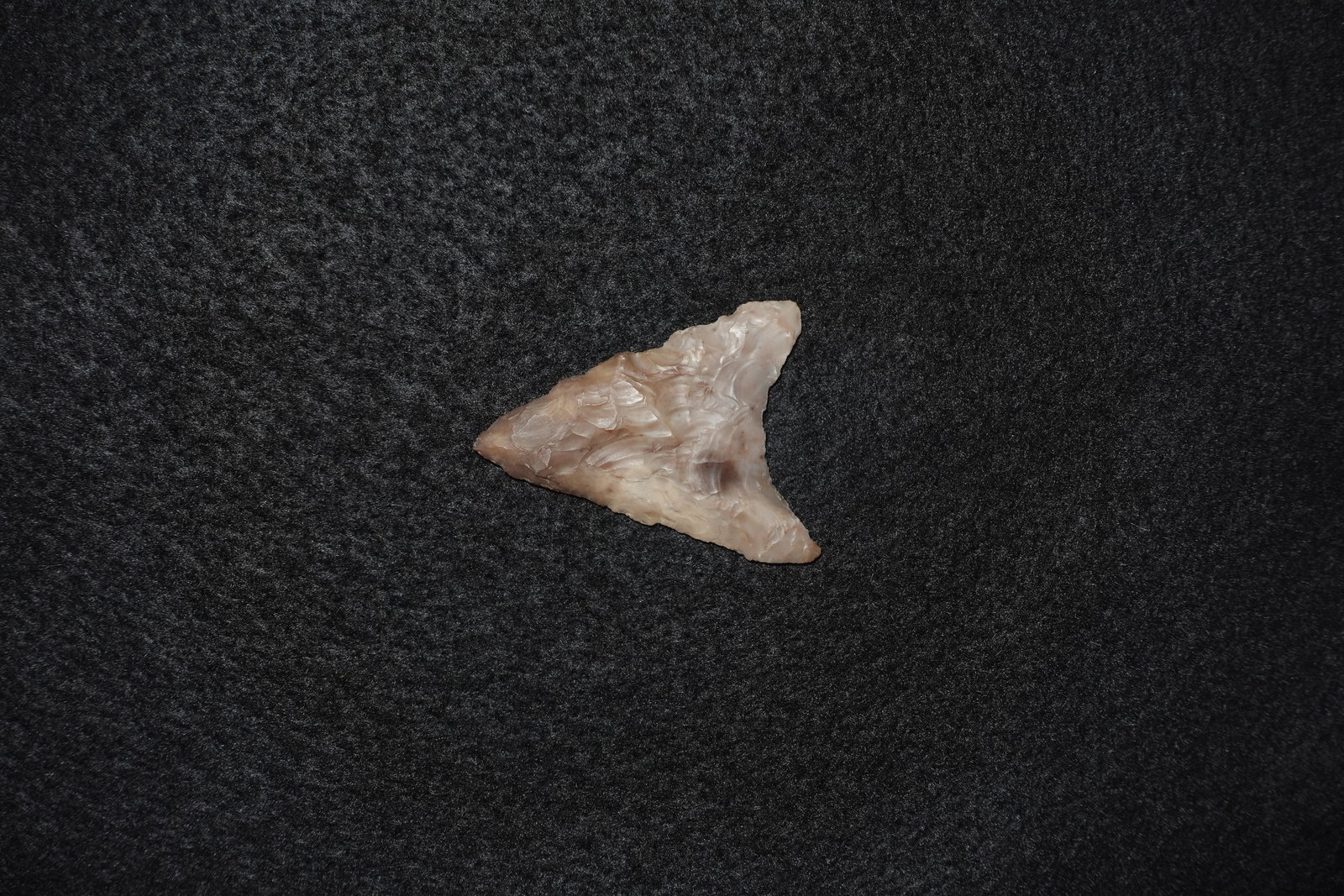 Mule Ear: Triangular flaked stone projectile point with pronounced basal 'mule-ear' projections and a broad triangular blade. Pale pink-beige translucent material with glossy areas and dense, overlapping flake