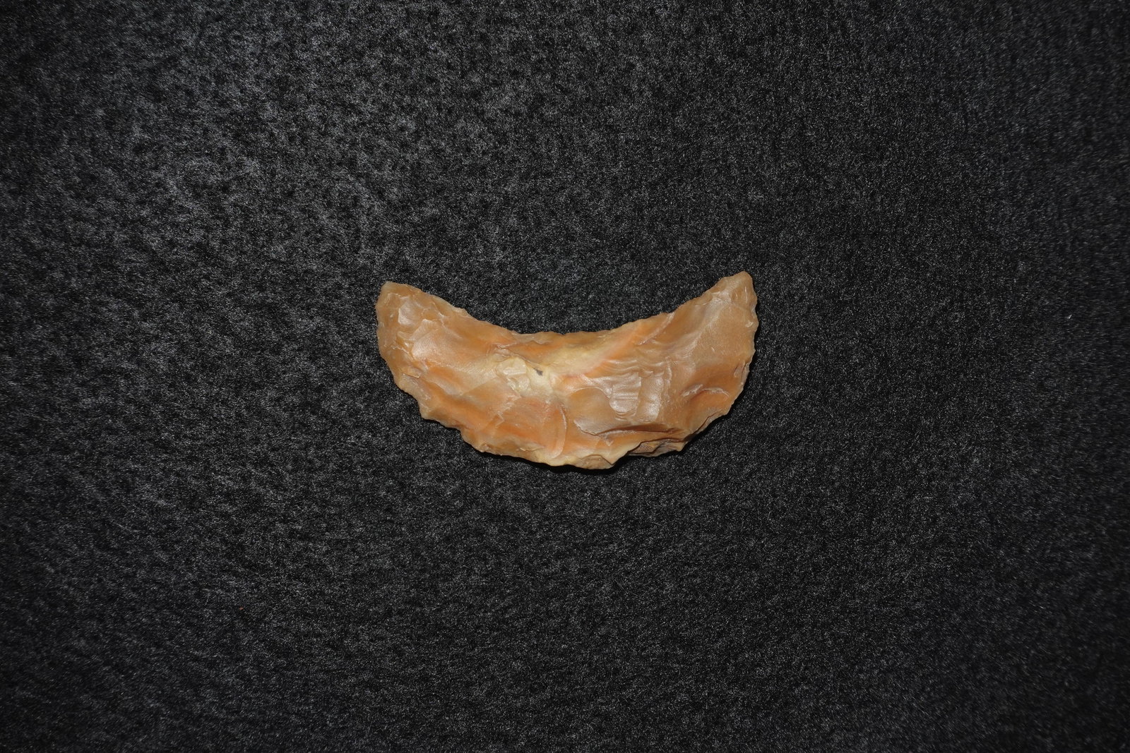 Butterfly Crescent blade: Crescent-shaped flaked stone blade made from a translucent orange-tan siliceous material with subtle banding. Bifacial knapping produced overlapping pressure-flake scars across the faces and a gently