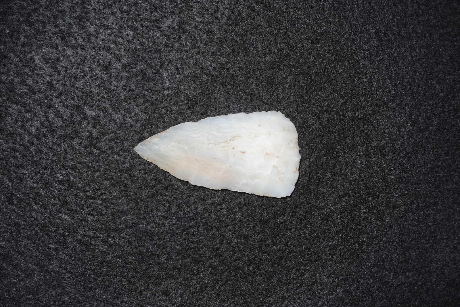 Agate Translucent Blade: Translucent white agate blade with a tapered triangular form and a sharp pointed tip. Finely pressure-flaked margins and stepped flake scars create a flaked, bifacial surface with subtle banding and