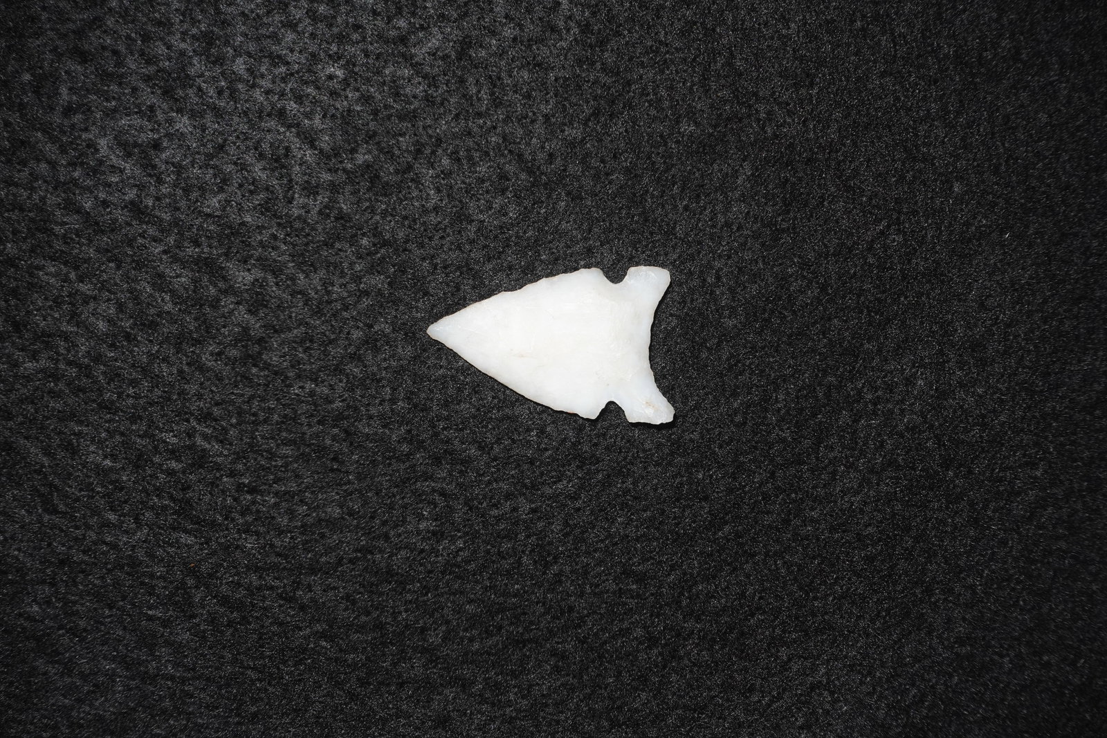 Avonlea Agate Point: White agate projectile point with a triangular, finely flaked blade and distinct basal notches. One face exhibits creamy tan staining and mineral deposits while the edges display percussion and