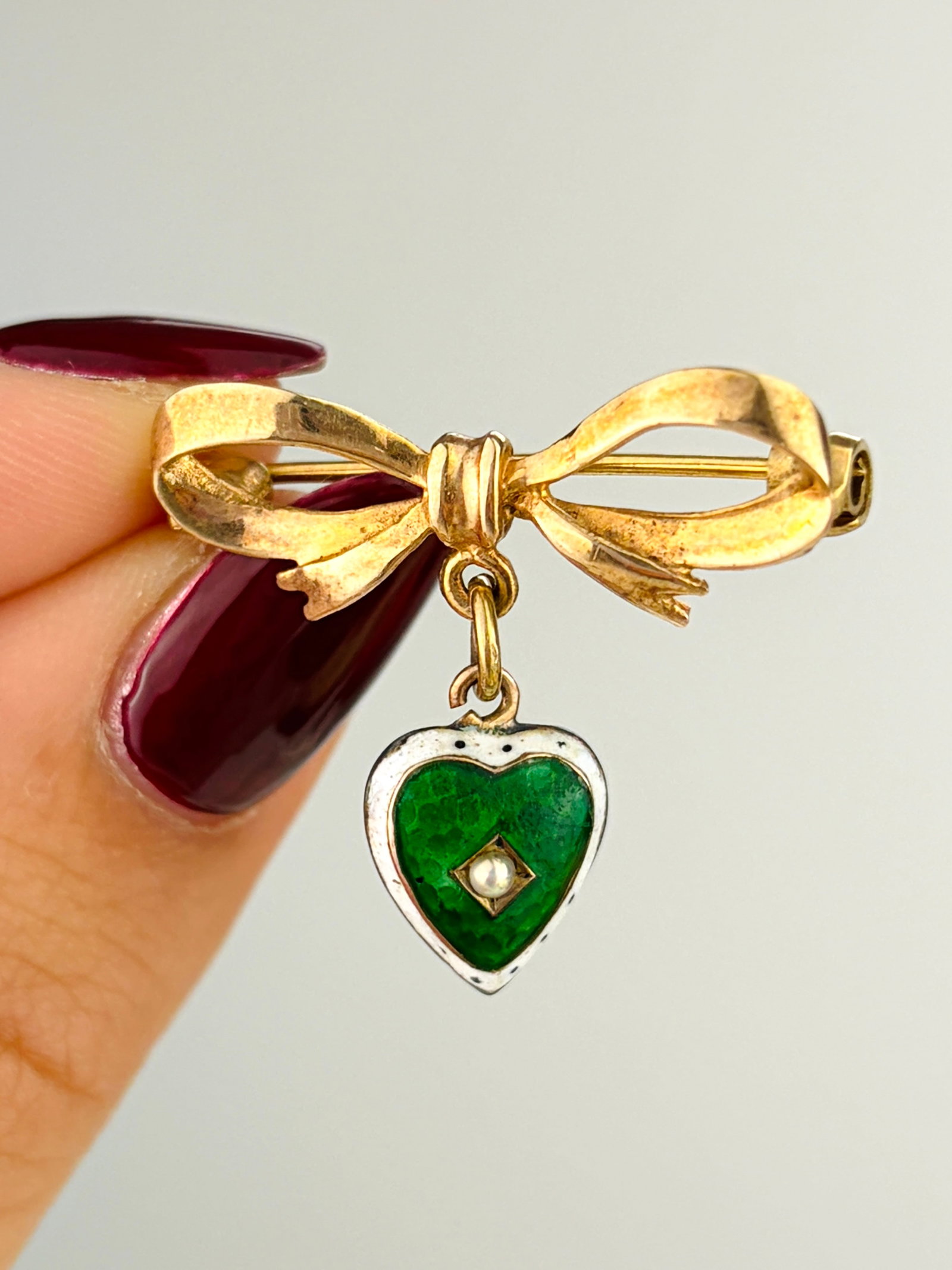 Sweet Antique Bow Brooch with Hanging Enamel Heart: Sweet Antique Bow Brooch with Hanging Enamel Heart Weight: 2.91g Size: 24x26mm Materials: 9ct Gold Hallmarks: Fully Hallmarked Condition: The overall condition is very good Office Use: DHZ The
