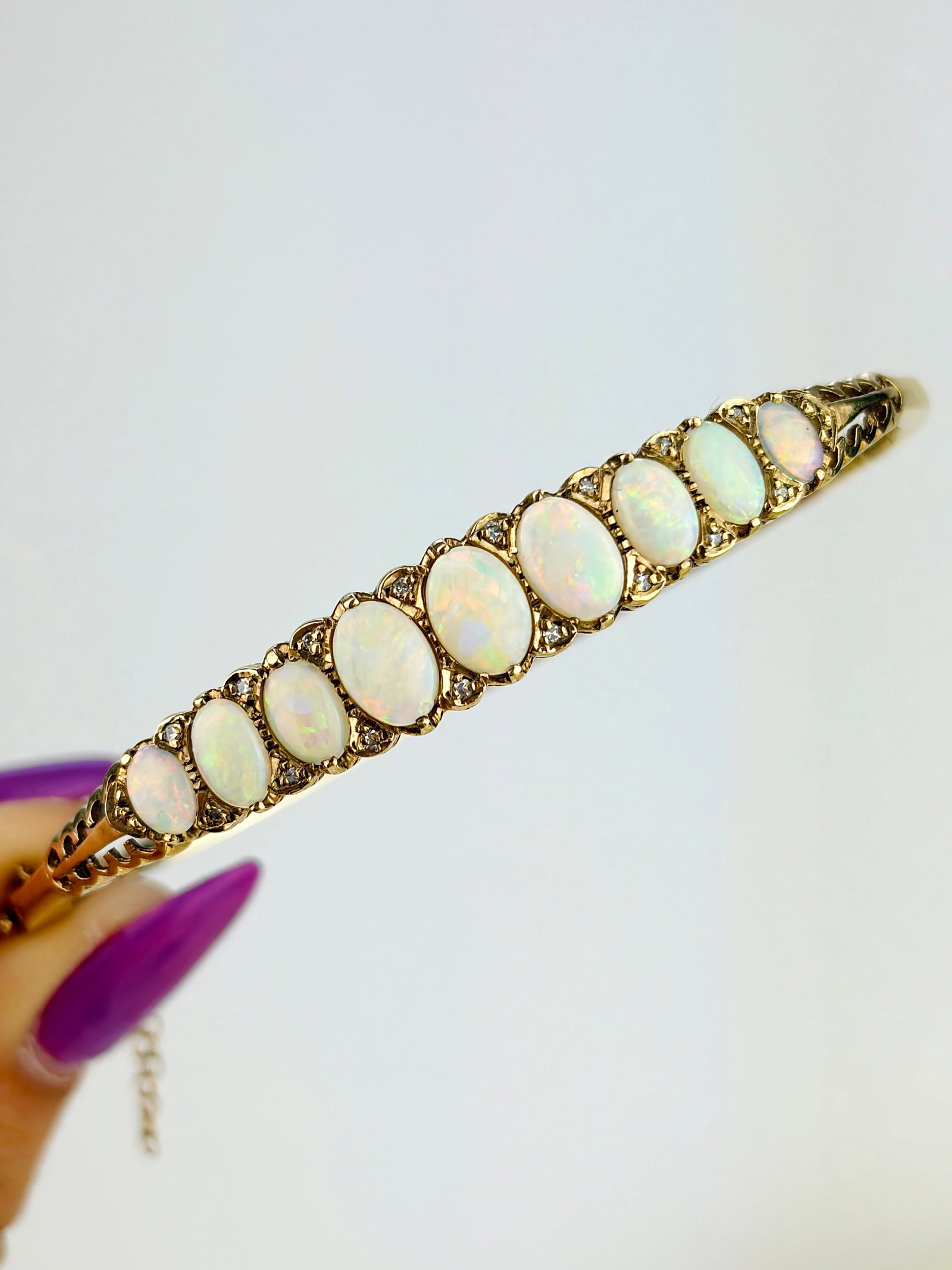 VINTAGE 9CT YELLOW GOLD OPAL AND DIAMOND BANGLE BRACELET: VINTAGE 9CT YELLOW GOLD OPAL AND DIAMOND BANGLE BRACELET A mesmerising bracelet featuring graduated cabochon opals that flash all kinds of stunning colours including oranges, pinks, blues, greens and