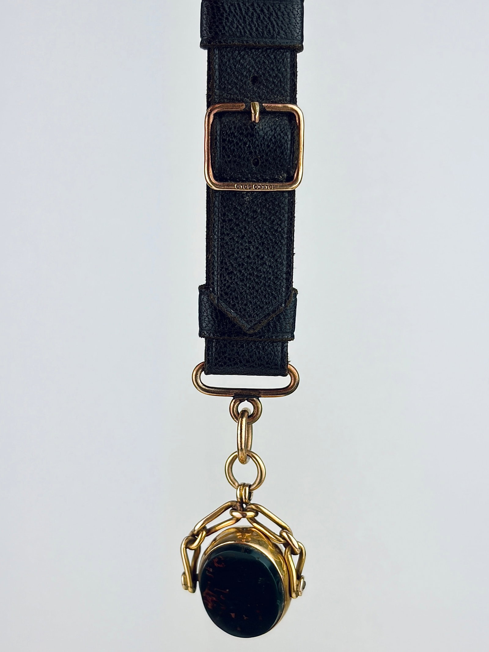 ANTIQUE CHUNKY 15CT GOLD SPINNING FOB SEAL PENDANT ON ANTIQUE LEATHER BRACELET: ANTIQUE CHUNKY 15CT GOLD SPINNING FOB SEAL PENDANT ON ANTIQUE LEATHER The fob is 15ct, and metal on the leather is rolled gold Weight: 11.87g Size: Fob 30x20mm, leather 95x15mm Materials: 15ct