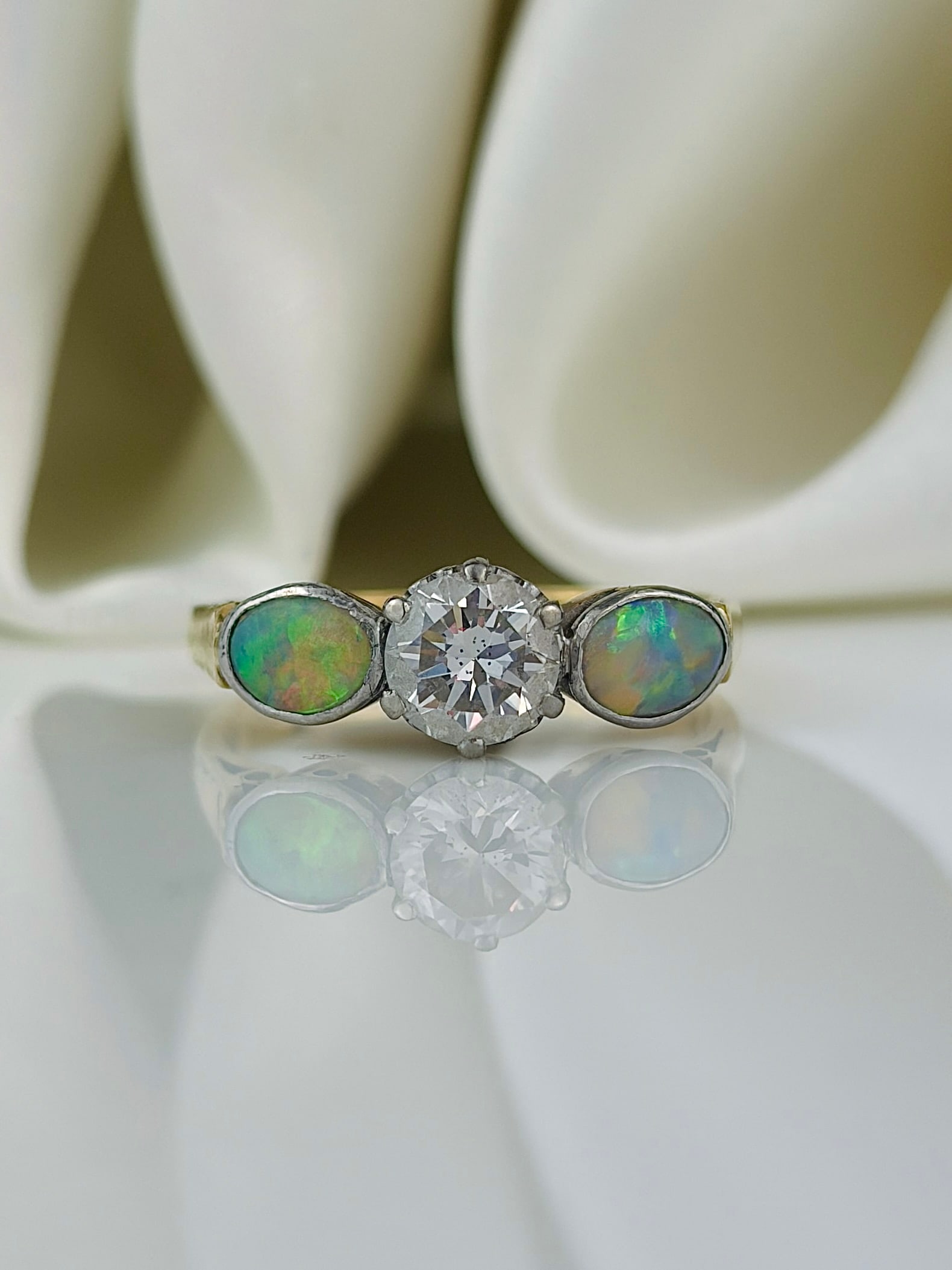Unusual black opal and 70pts diamond 3 stone ring in 18ct yellow gold and platinum: Unusual black opal and 70pts diamond 3 stone ring in 18ct yellow gold and platinum A beautiful .70pts diamond complimented either side by the brightest, most colourful opal stones! Weight: 3.1g Size: