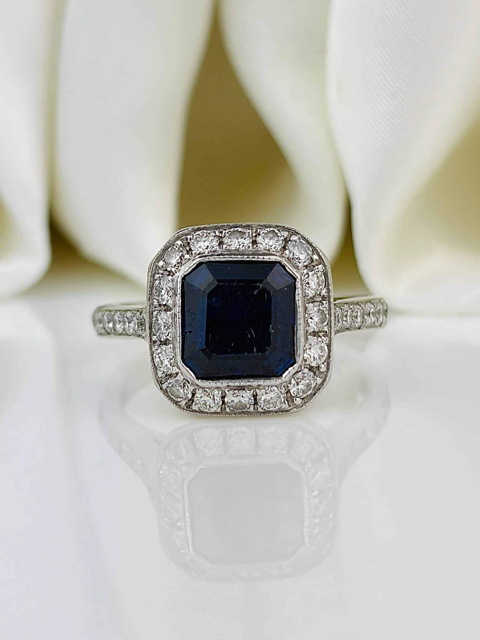 Vintage Sapphire and Diamond Encrusted 18ct White Gold Panel Ring: Vintage Sapphire and Diamond encrusted 18ct White Gold Panel Ring This ring is gorgeous and holds an inky blue sapphire at the centre of a halo of sparkling diamonds. The sapphire measures 75pts and t