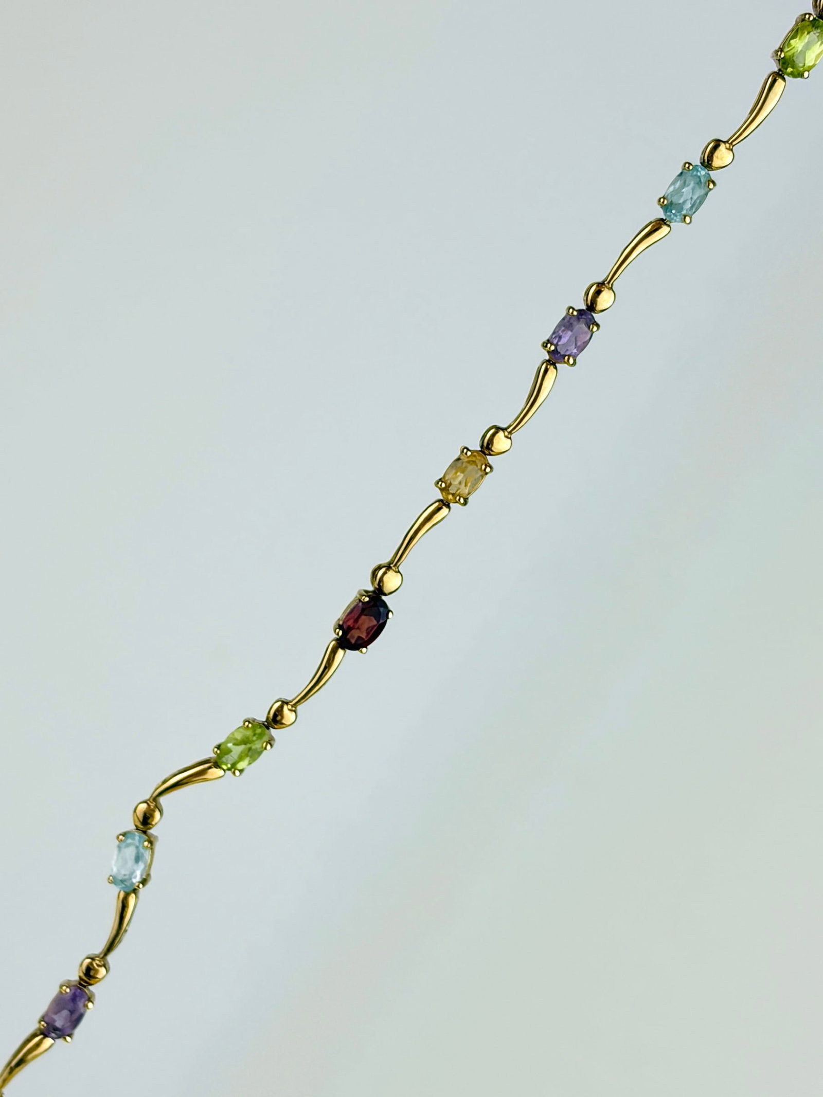 Vintage 9ct Yellow Gold Multigem Flowing Link Bracelet: Vintage 9ct Yellow Gold Multigem Flowing Link Bracelet A gorgeous bracelet featuring peridot, garnet, citrine, amethyst, and topaz. There is one part of the flowing design that has a more exaggerated