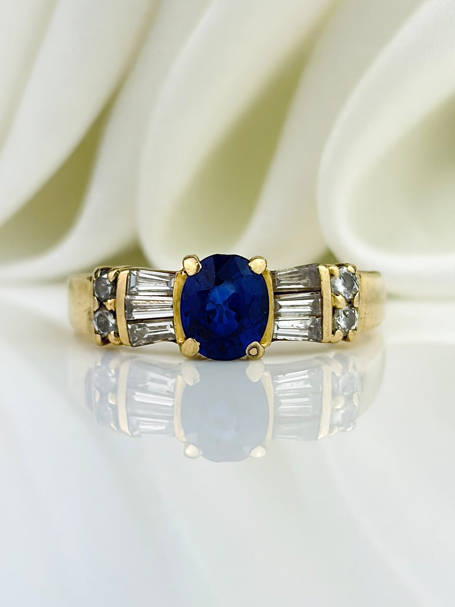VINTAGE 18CT YELLOW GOLD SAPPHIRE AND DIAMOND BAGUETTE SHOULDER RING: VINTAGE 18CT YELLOW GOLD SAPPHIRE AND DIAMOND BAGUETTE SHOULDER RING Captivating ring featuring a bright central sapphire flanked by baguette cut diamonds on either side!