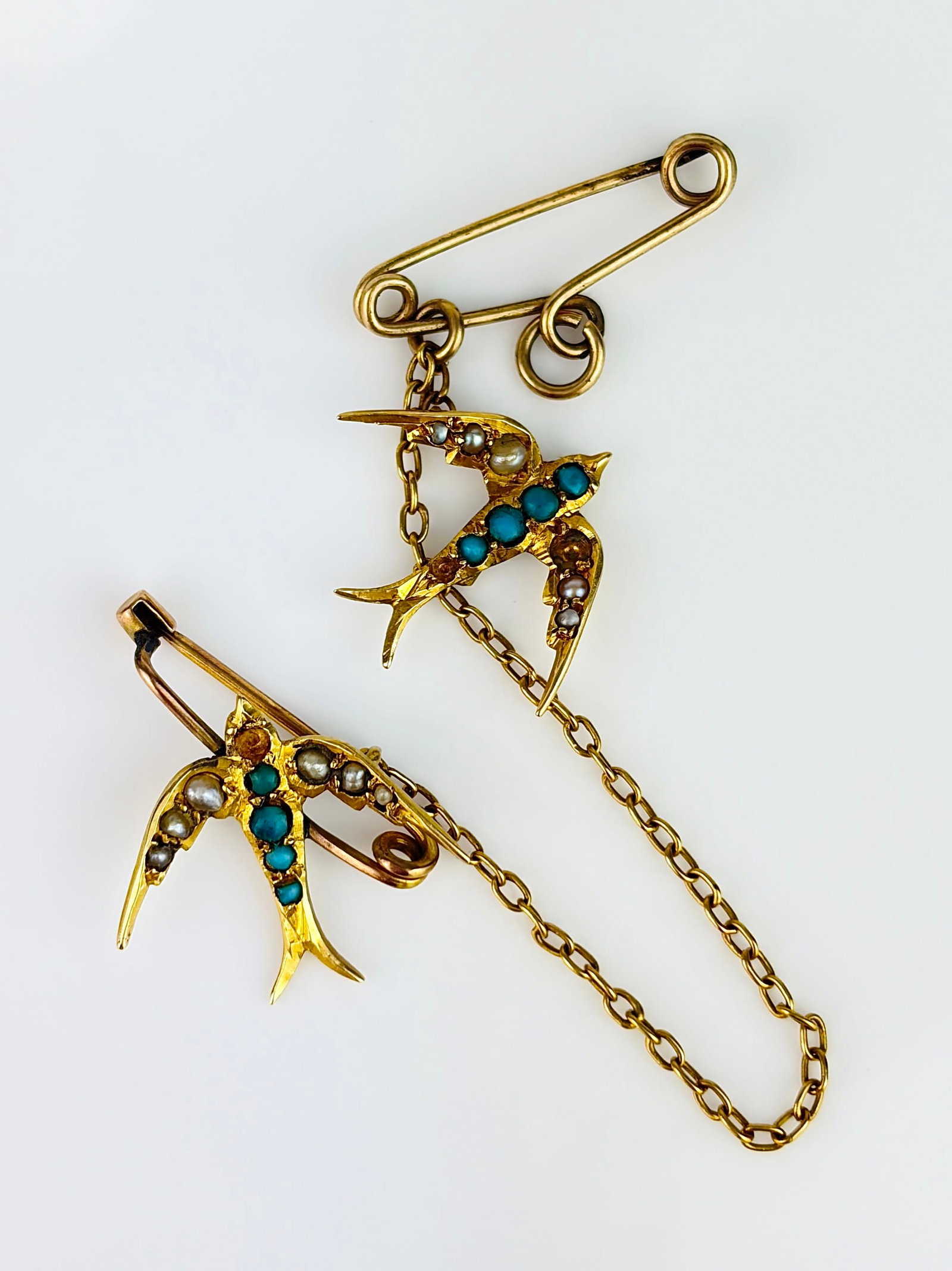 ANTIQUE 15CT YELLOW GOLD DOUBLE TURQUOISE AND PEARL SWALLOW BIRD BROOCH: ANTIQUE 15CT YELLOW GOLD DOUBLE TURQUOISE AND PEARL SWALLOW BIRD BROOCH Two sweet swallow birds adorned with turquoise bodies and pearl wings, on separate brooches, but connected by a safety chain! On