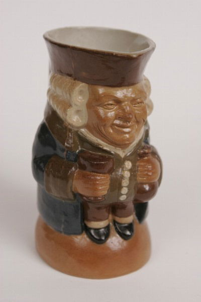 Doulton Lambeth Toby Jug: Molded in stoneware as a standing toby, wearing a blue coat, olive green waistcoat, and brown trousers, impressed with Royal Doulton Lambeth mark surmounted by a lion, "SM". 6 1/4"H. Condition: large