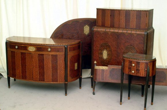 Robert Irwin Art Deco Suite: Comprising; a full size headboard and footboard, demi-lune commode, bed side stand, and chest of drawers, and mirror, each inlaid with burled veneers and ivory simulant floral medallions, applied with