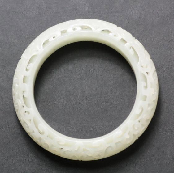 Chinese White Jade Bangle Bracelet: Chinese white jade bangle bracelet, the rounded exterior carved of open works of floral and with antiques precious objects, the semi-translucent pale celadon white. 3" x 3".