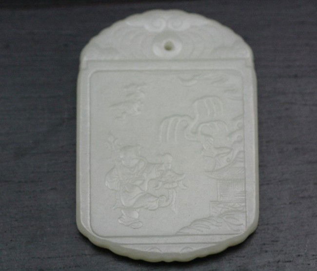 Chinese White Jade Pendant: A Chinese carved white jade pendant, of oval shape, finely carved in low relief with a boy playing in a celestial landscape, the top and bottom border carved with wave designs. 2" x 1.3".