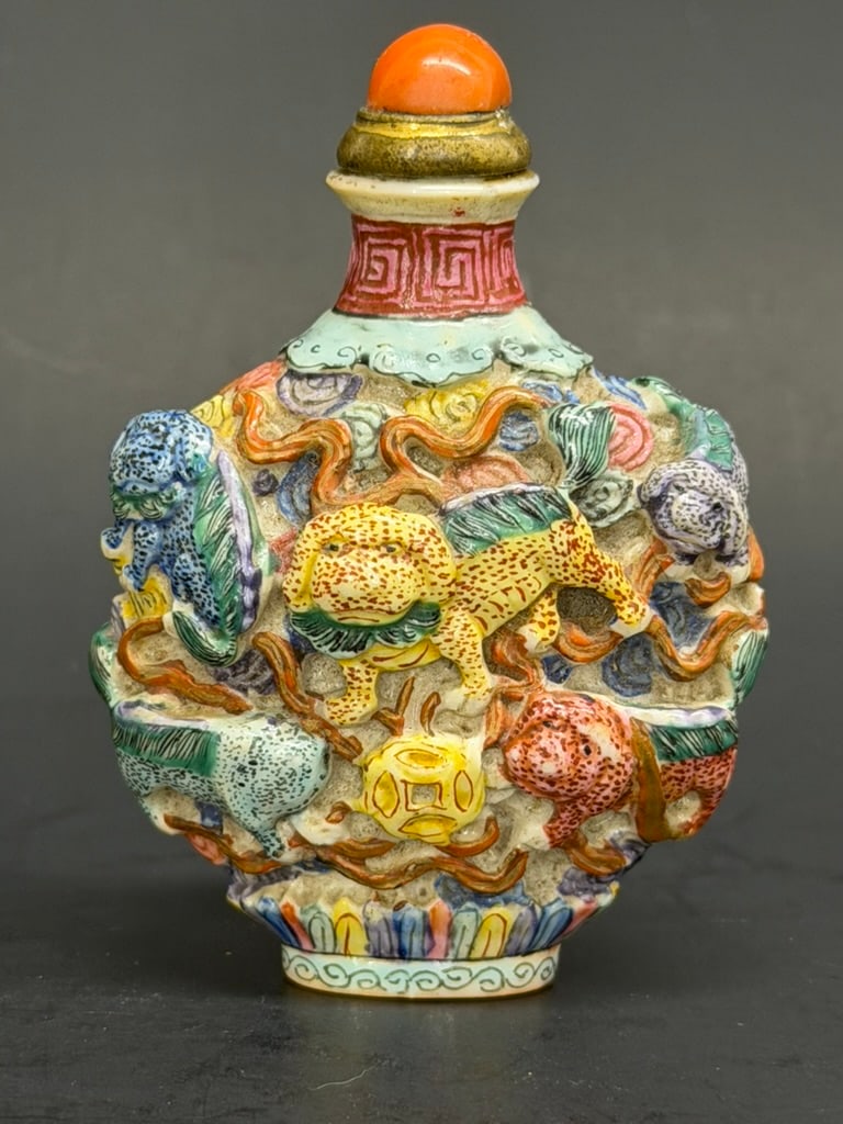 Chinese Qing Dynasty Famille Rose “Nine Buddhist Lions" molded porcelain snuff bottle with a red co: This item is a fine 19th Century Qing Dynasty Famille Rose molded porcelain snuff bottle of flattened ovoid form with a wasted neck, a flat gilded lip, and an oval concave foot. The body of the bottle