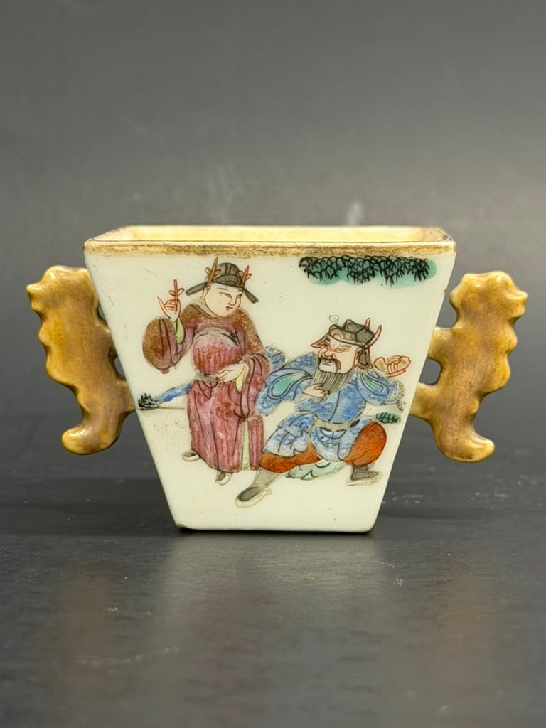Chinese Late Qing Famille Rose Square Handled cup Douguang Reign Mark: Chinese Late Qing Famille Rose Square Handled cup Douguang Reign Mark. 6 Hand painted figures amongst trees and flowers decorate the sides and 2 gilt stylized temple lion handles. 1 5/8" tall by 3 1/8